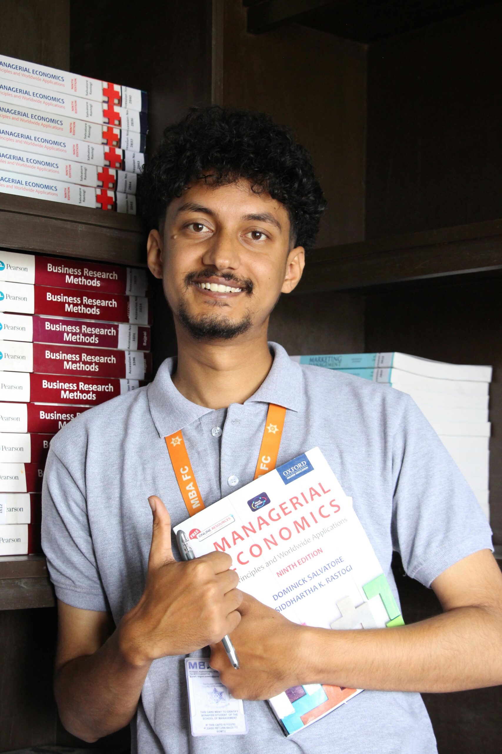 A student holding a textbook on Managerial Economics, smiling in a college library.
